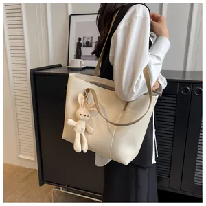Close-up of beige tote bag with shoulder strap and plush rabbit charm for daily office use