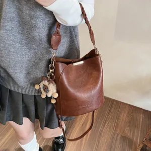 Retro braune Beuteltasche mit gewebtem Griff und Plüschbär-Anhänger am Modell
