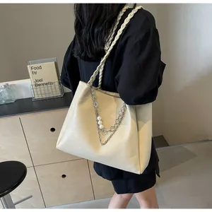 Close-up of beige tote bag with woven shoulder straps and pearl chain decorative pendant