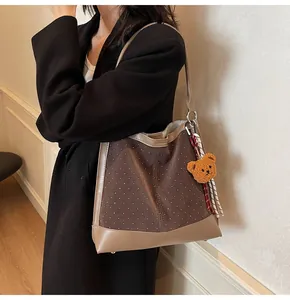 Detail of suede tote bag with brown textures, metal studs and a cute plush bear charm