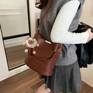 Braune geflochtene Eimer-Tasche mit Löwen-Anhänger als stilvolle Umhängetasche an einem Model