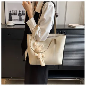Detail of a beige tote bag with a long strap, rabbit charm, and Fashion Trend text