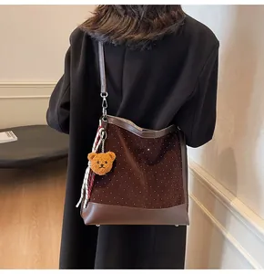 Detail of dark brown suede bucket bag with plush bear charm and plaid scarf accent