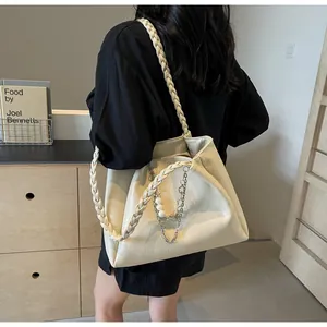 Detail of cream tote bag featuring woven straps and decorative pearl metal chain link