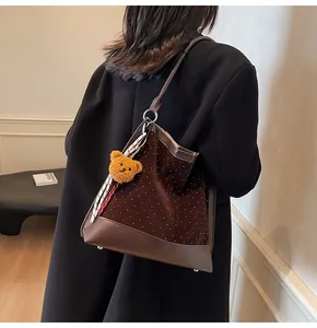 Detail of suede shoulder bag with polka dots, leather trim, and a bear charm pendant