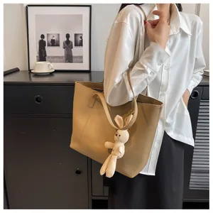 Khaki leather tote bag detail with cream plush bunny charm in a lifestyle interior