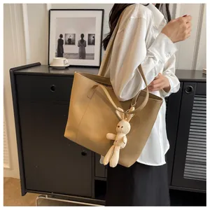 Detail of light brown leather tote bag with a cute white rabbit plush charm pendant