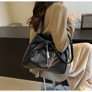 Detail of black tote bag with woven shoulder strap and decorative pearl chain charm