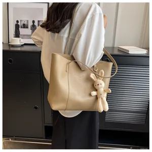 Detail of khaki tote bag with plush rabbit charm and elegant shoulder strap design
