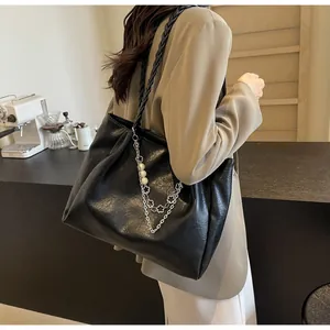Detail of black pleated tote bag with woven shoulder strap and pearl charm accessory
