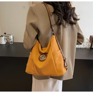 Detailaufnahme der gelben Beuteltasche mit M-Logo aus Metall und braunem Leder-Schultergurt