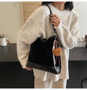Polka dot suede shoulder bag with bear charm shown worn over a knitted sweater