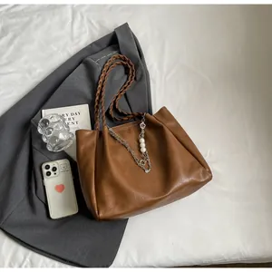 Detail of brown tote bag featuring woven straps, metal chains, and pearl charms