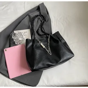 Detail of black ruched tote bag with woven handles and pearl chain decorative charms