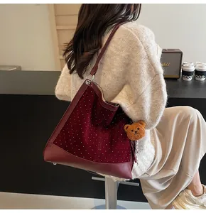 Detail of burgundy suede shoulder bag with silver studs and plush bear charm on model