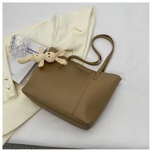 Brown tote bag detail with gold logo and plush rabbit charm on a minimalist setup