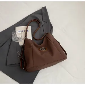 Detail einer braunen matten Schultertasche mit Metalllogo neben einem Blazer