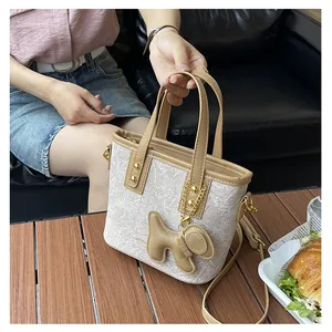 Details einer schicken cremefarbenen Mini-Tote-Bag mit braunem Lederbesatz und Anhänger