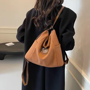 Minimalistische braune Umhängetasche aus Kunstleder mit silbernem M-Logo auf Model