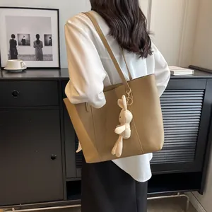 Minimalist khaki leather tote bag with plush rabbit charm shown on model shoulder