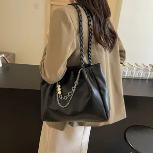Black PU leather tote bag with woven shoulder strap and pearl chain charm on model