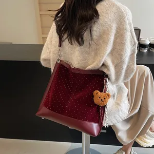 Polka dot burgundy suede tote bag with plush bear charm in a lifestyle cafe setting