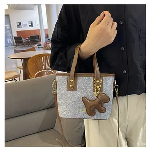 Detail der grauen Stoff-Beuteltasche mit braunem Lederbesatz und Welpenanhänger