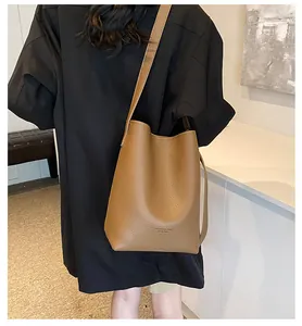 Detail view of brown pebbled leather bucket bag with debossed fashion logo on a model