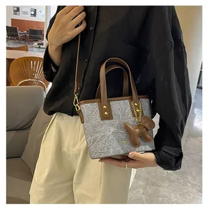 Tragebild einer Eimer-Handtasche mit Marmormuster, braunen Griffen und Bärenanhänger