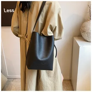 Detail shot of black pebbled leather bucket bag styled with a minimalist beige trench coat