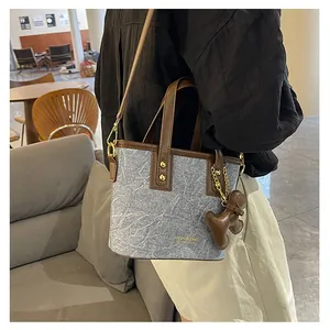 Detail der grauen Bucket Bag mit braunen Ledergriffen und süßem Bären-Anhänger