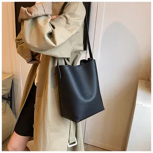 Detail of a black pebbled leather bucket bag styled with a trench coat for daily fashion