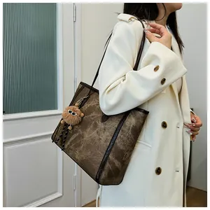 Detail of a large vintage brown tote bag with leather straps and a fuzzy charm