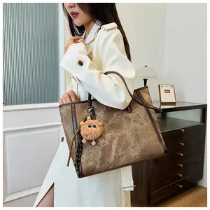 Close-up of a large brown canvas tote bag with leather trim and a plush ball charm