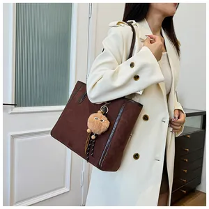 Detail of a brown suede tote bag with leather trim and a beige plush eye pendant