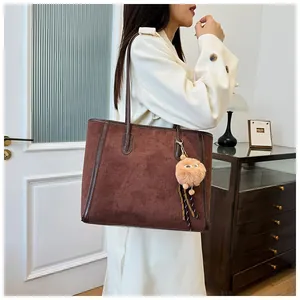 Close-up of matte brown tote bag with glossy leather trim and plush ball charm accessory