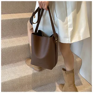 Deep brown bucket bag in pebbled leather with adjustable strap shown on a model