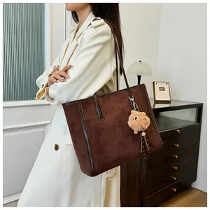 Brown suede tote bag with leather trim and pompom detail on white coat model