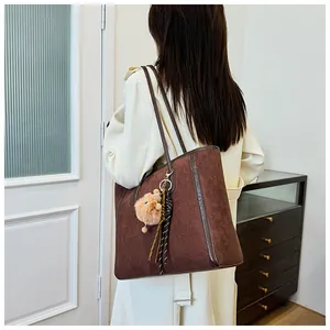 Close-up of large brown suede tote bag with leather handles and cute bear charm detail