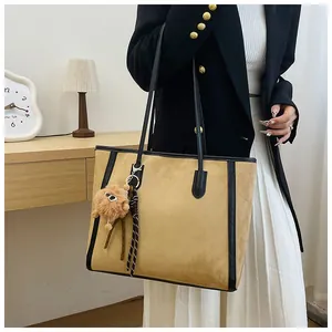 Detail of khaki tote bag with black trim and plush charm in a stylish indoor setting