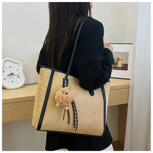 Detail of large camel tote bag in suede texture with black leather trim and plush charm