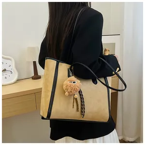 Close-up of beige suede tote bag with black leather trim and cute plush ball charm
