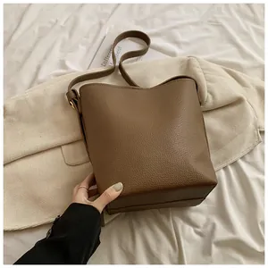 Detail of dark brown bucket bag with lychee texture and adjustable strap on white sheets