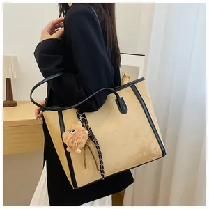 Detail of beige suede tote bag with black leather trim and cute plush ball charm accessory