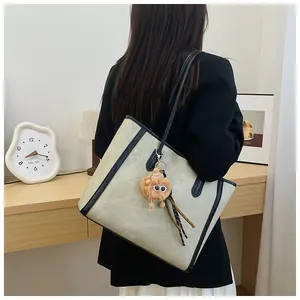 Detailed back view of a beige tote bag with black trim and a plush charm on a model