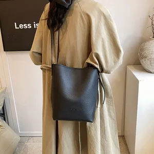 Minimalist black pebble leather bucket bag with long strap shown in a modern lifestyle setting