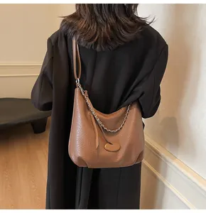 Vista laterale di una borsa hobo in pelle marrone con catena d'argento su una modella