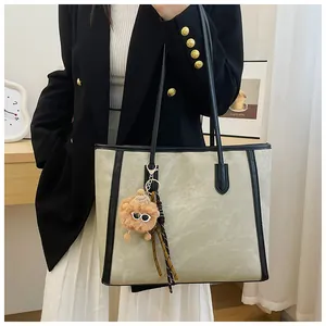 Detail of light green tote bag with plush monster charm and reinforced black straps