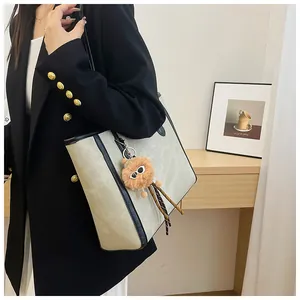 Light gray tote bag with black trim and brown plush charm shown on a shoulder
