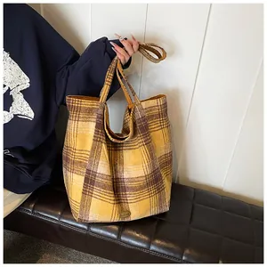 Close-up of yellow and brown plaid tote bag showing tweed texture and metal logo plate